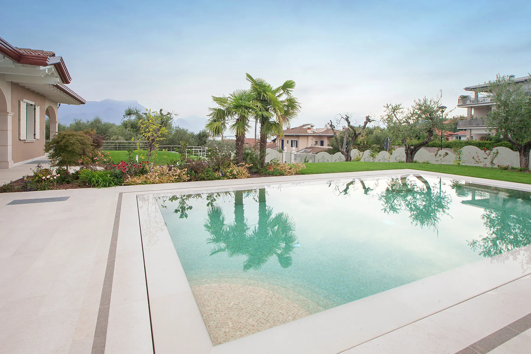 Piscine rectangulaire avec margelles en pierre claire et reflets de palmiers dans l'eau