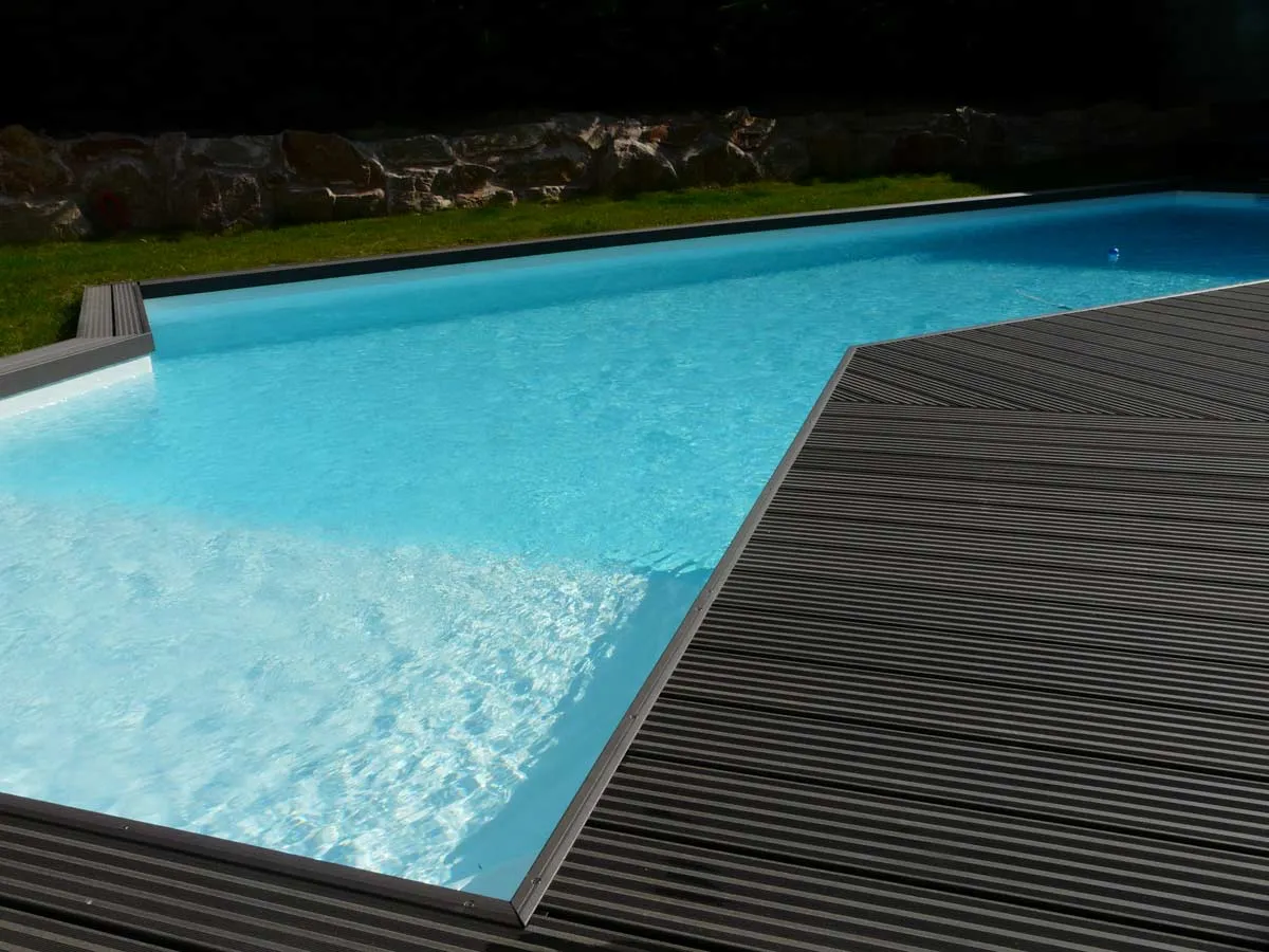 Piscine en L avec terrasse composite et mur en pierre — réalisation Beaulieu Piscines